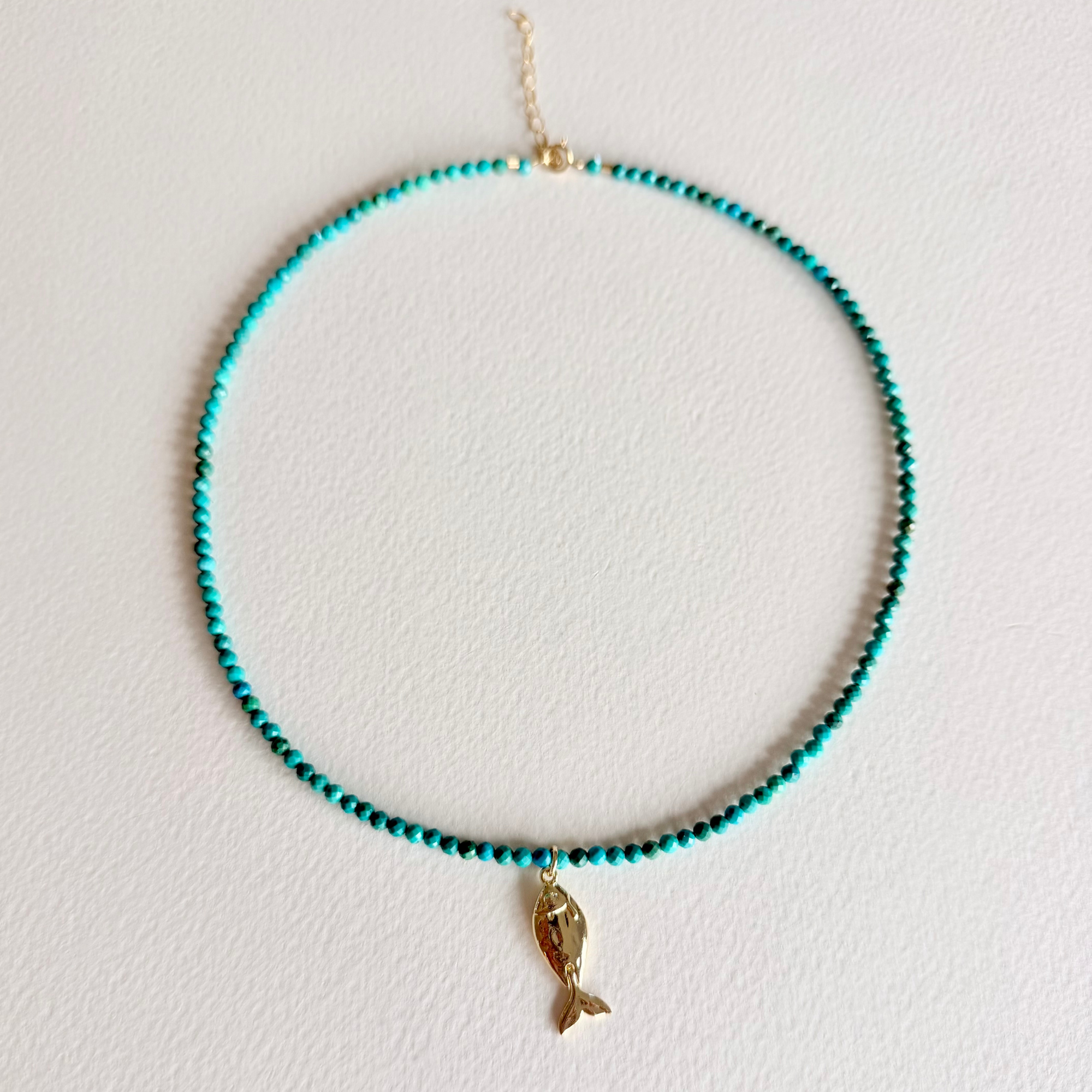 turquoise beaded necklace with a fish charm on light background