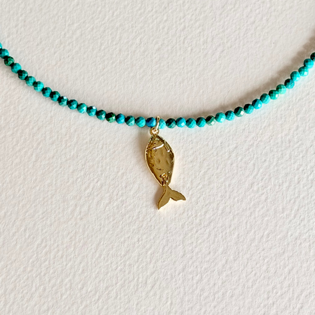 turquoise beaded necklace with a fish charm close up on light background