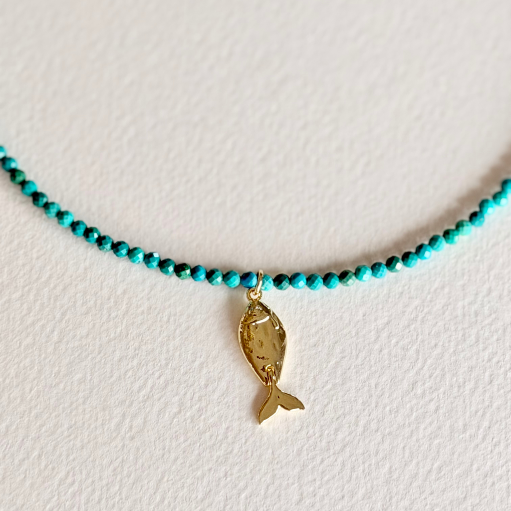 turquoise beaded necklace with a fish charm close up on light background
