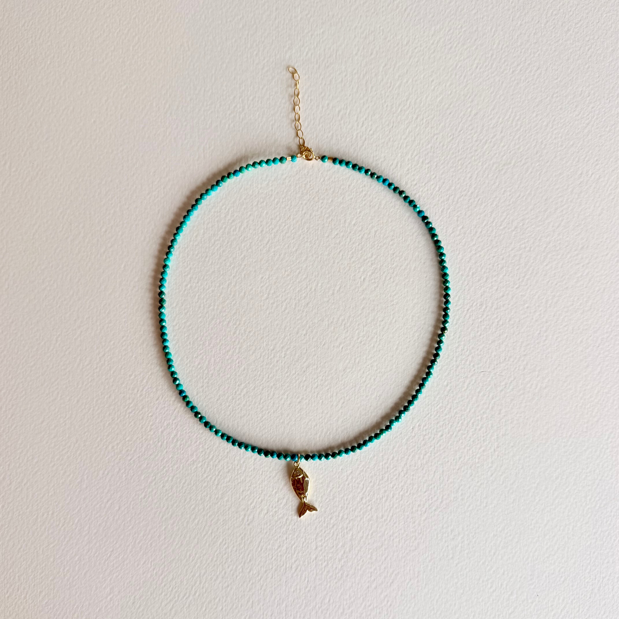 turquoise beaded necklace with a fish charm on light background