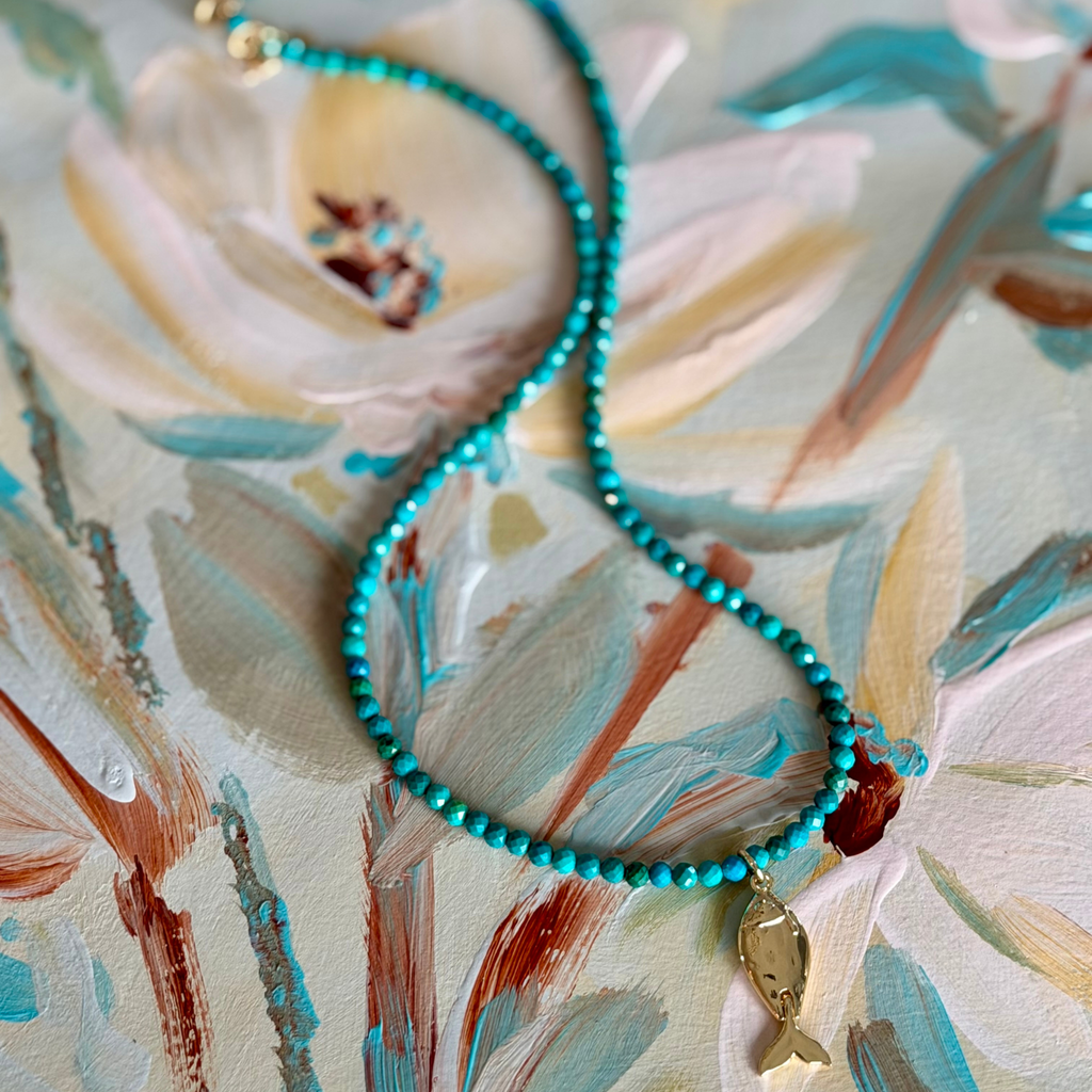 turquoise beaded necklace with a fish charm on a magnolia painting