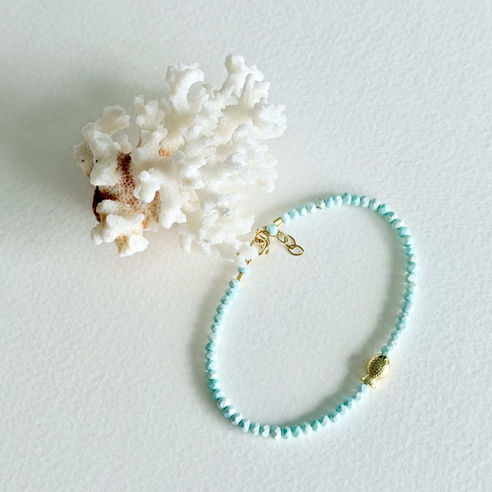 Turquoise beaded bracelet with gold clasp on a light gray background with white coral.