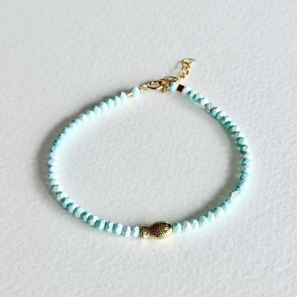 Turquoise beaded bracelet with a gold clasp on a light gray background
