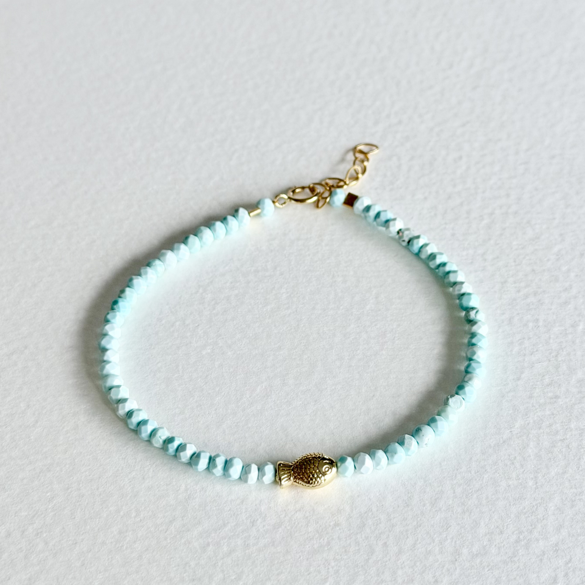Turquoise beaded bracelet with a gold fish charm on a light gray background