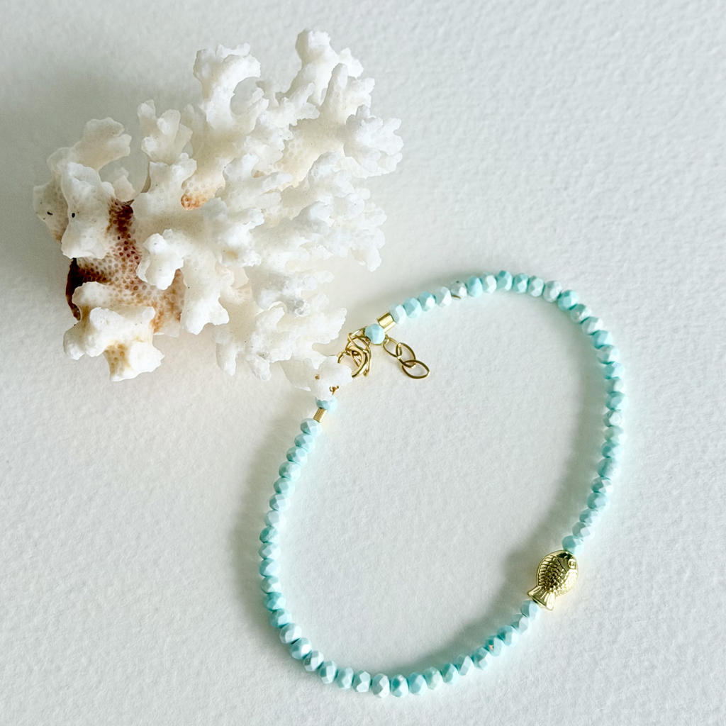 Turquoise beaded bracelet with gold fish charm on a white background