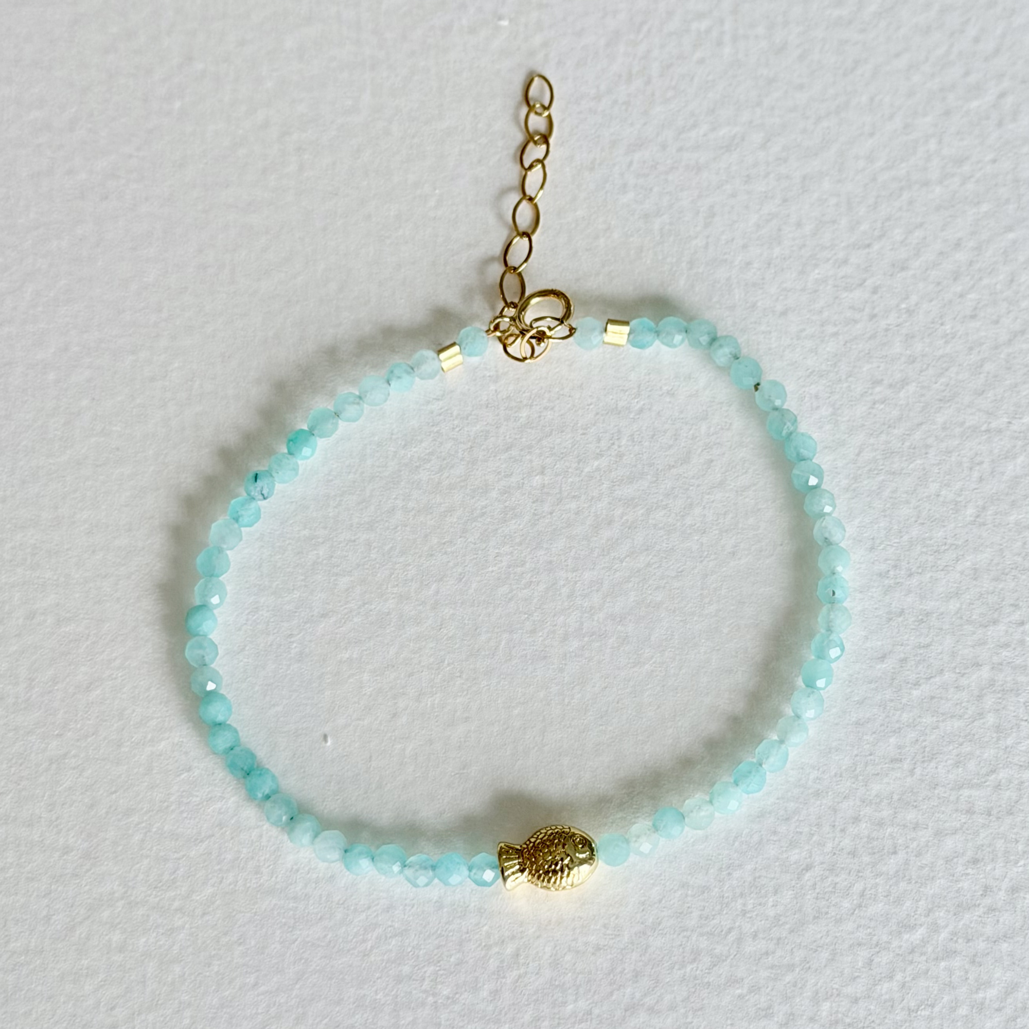 Turquoise beaded bracelet with a gold fish charm on a light gray background