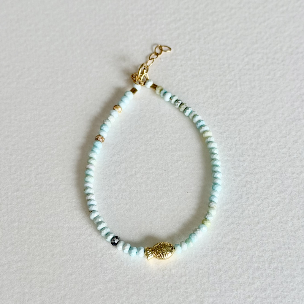 Beaded bracelet with gold fish charm on a light gray background