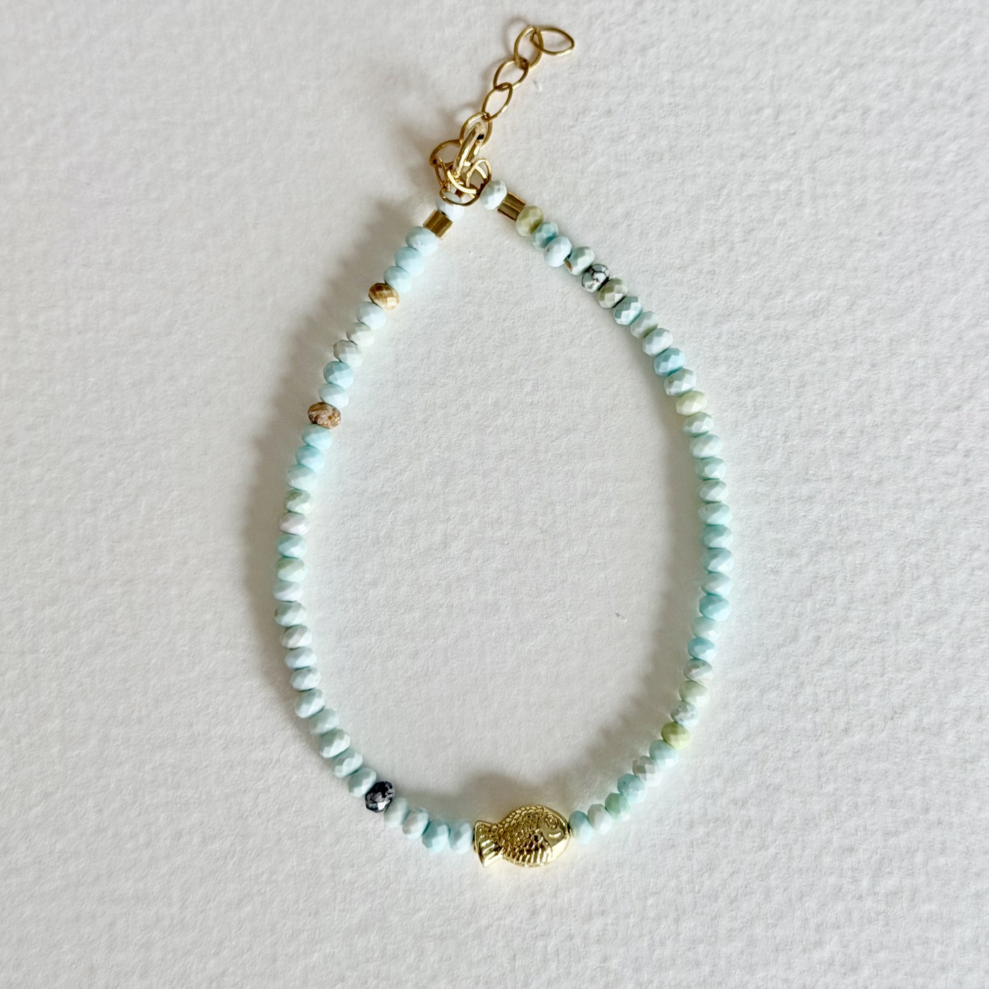 Beaded bracelet with a gold fish charm on a light background