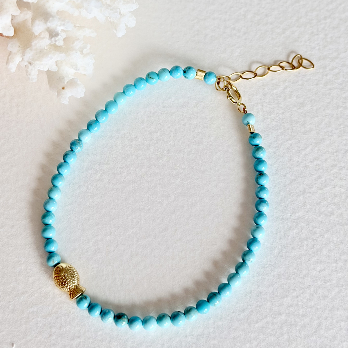 Turquoise beaded bracelet with gold accents on a textured white surface