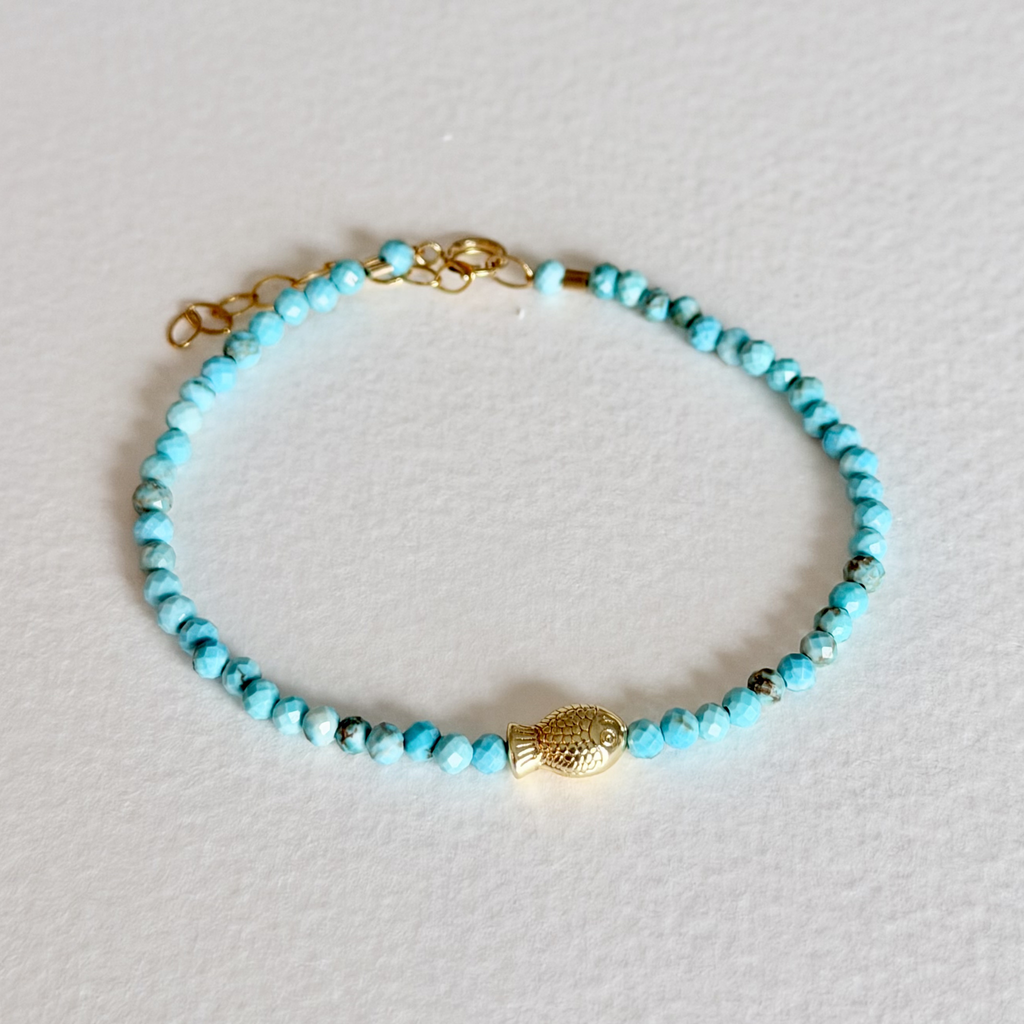 Turquoise beaded bracelet with a gold clasp on a light gray background