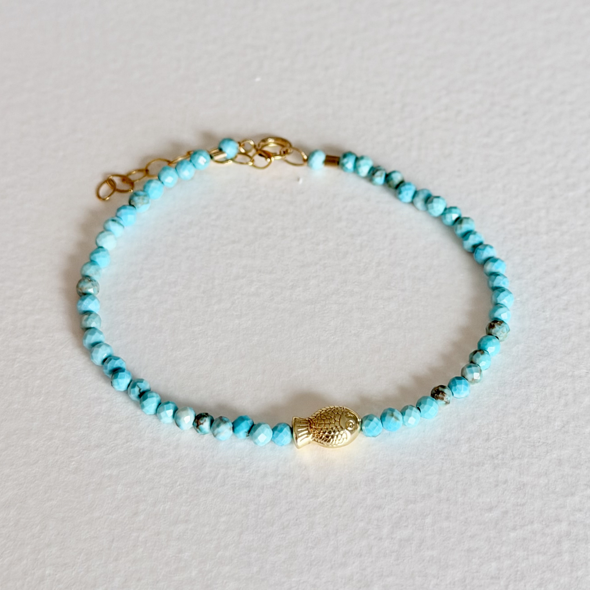 Turquoise beaded bracelet with a gold clasp on a light gray background