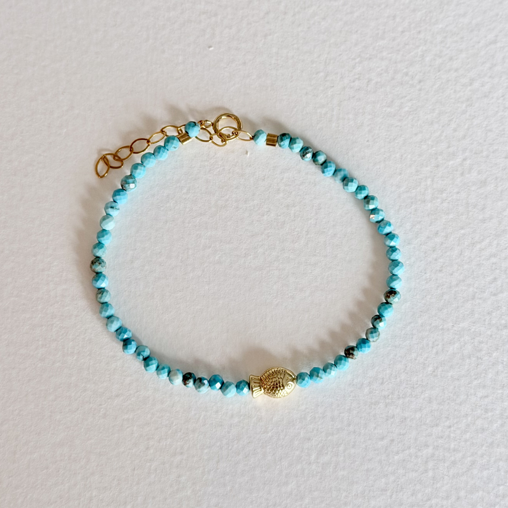 Turquoise beaded bracelet with gold accents on a light gray background