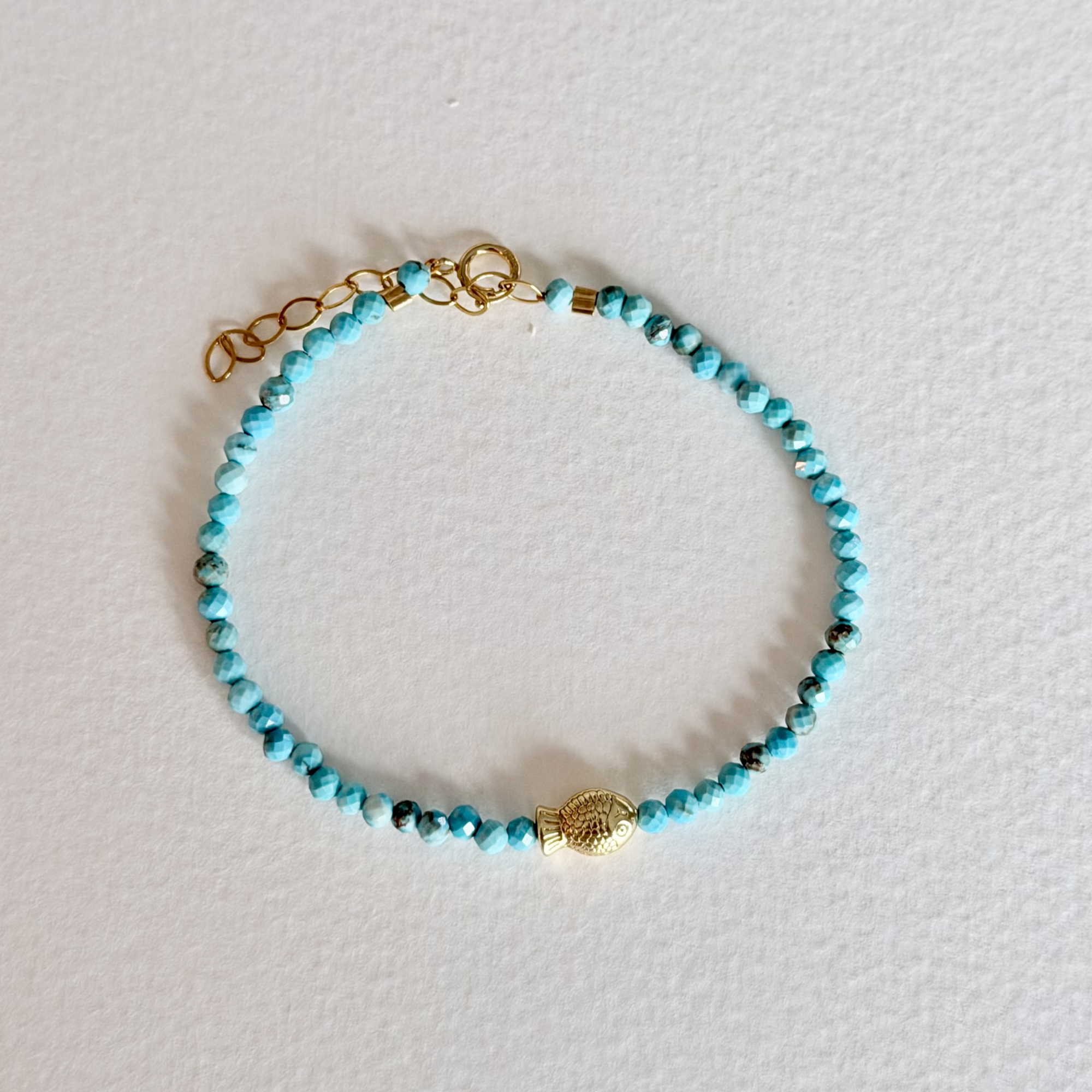 Turquoise beaded bracelet with gold accents on a light gray background