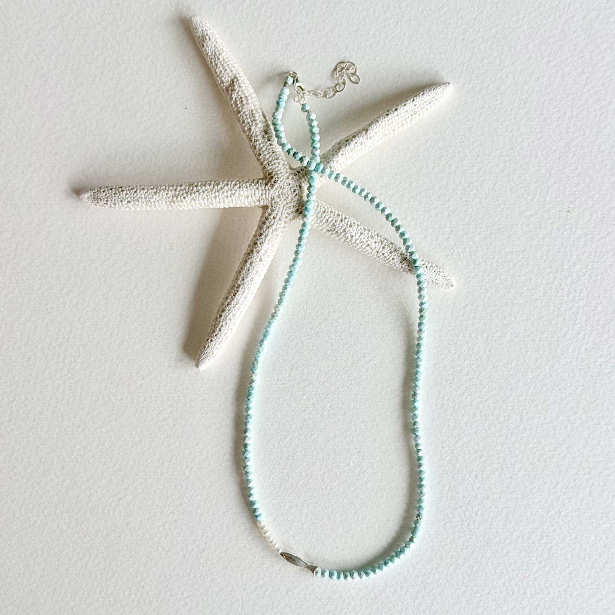 A delicate mint green beaded necklace with a silver lobster clasp, displayed on a white starfish prop against a clean white background.