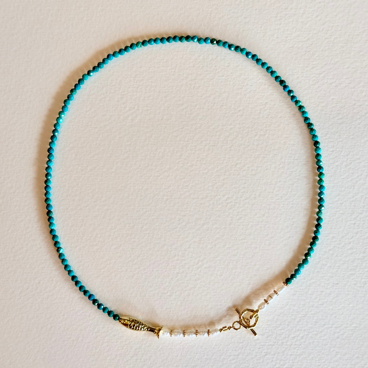 Turquoise beaded necklace with gold clasp on a light background
