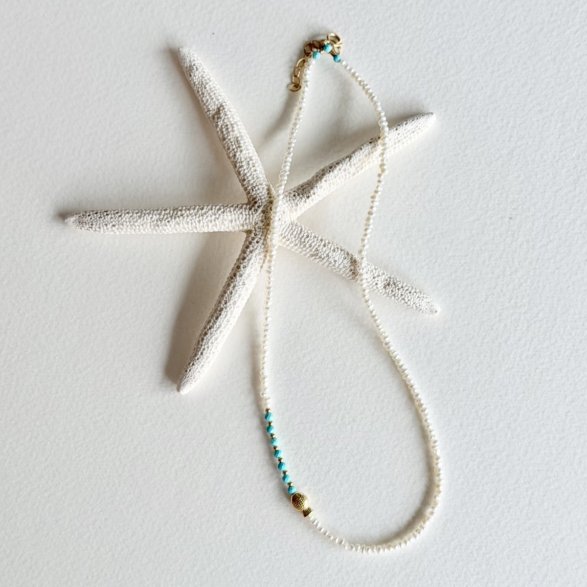 A textured white starfish-shaped pendant necklace with a delicate white beaded chain and small turquoise and gold bead accents, displayed on a clean white background.