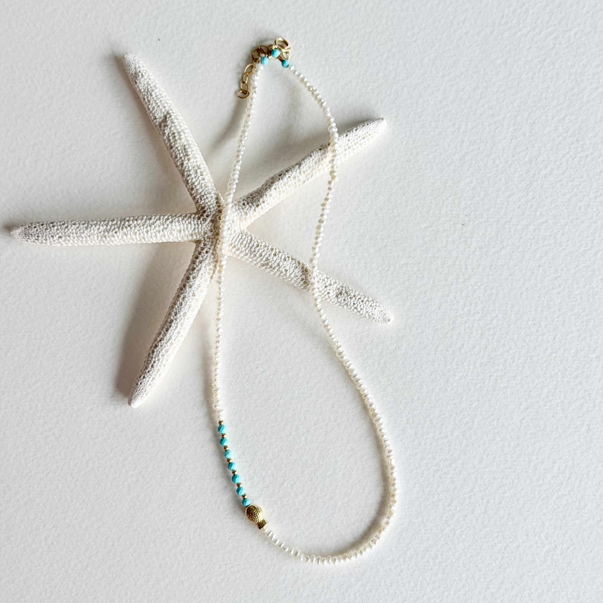 A white textured starfish-shaped pendant necklace with a matching beaded chain featuring turquoise and gold beads, displayed on a white background.