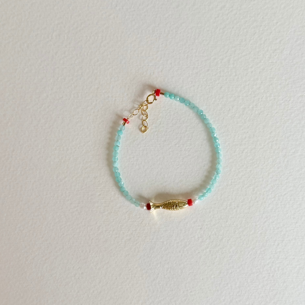 Beaded bracelet with gold charm on a light gray background