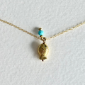 A delicate gold chain necklace featuring a small fish-shaped pendant and a single turquoise bead, displayed on a textured white background.