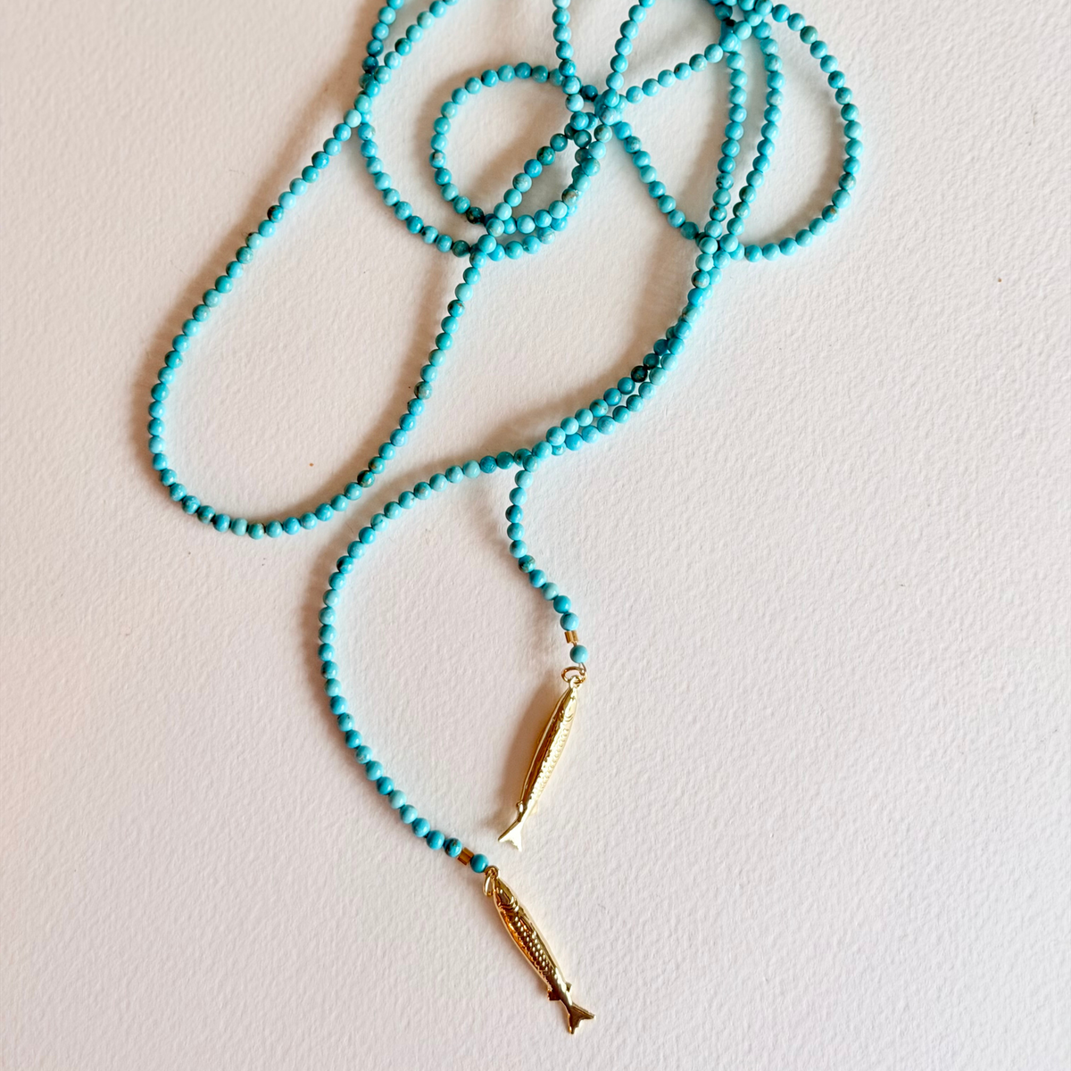 Turquoise beaded necklace with a gold clasp on a light pink background