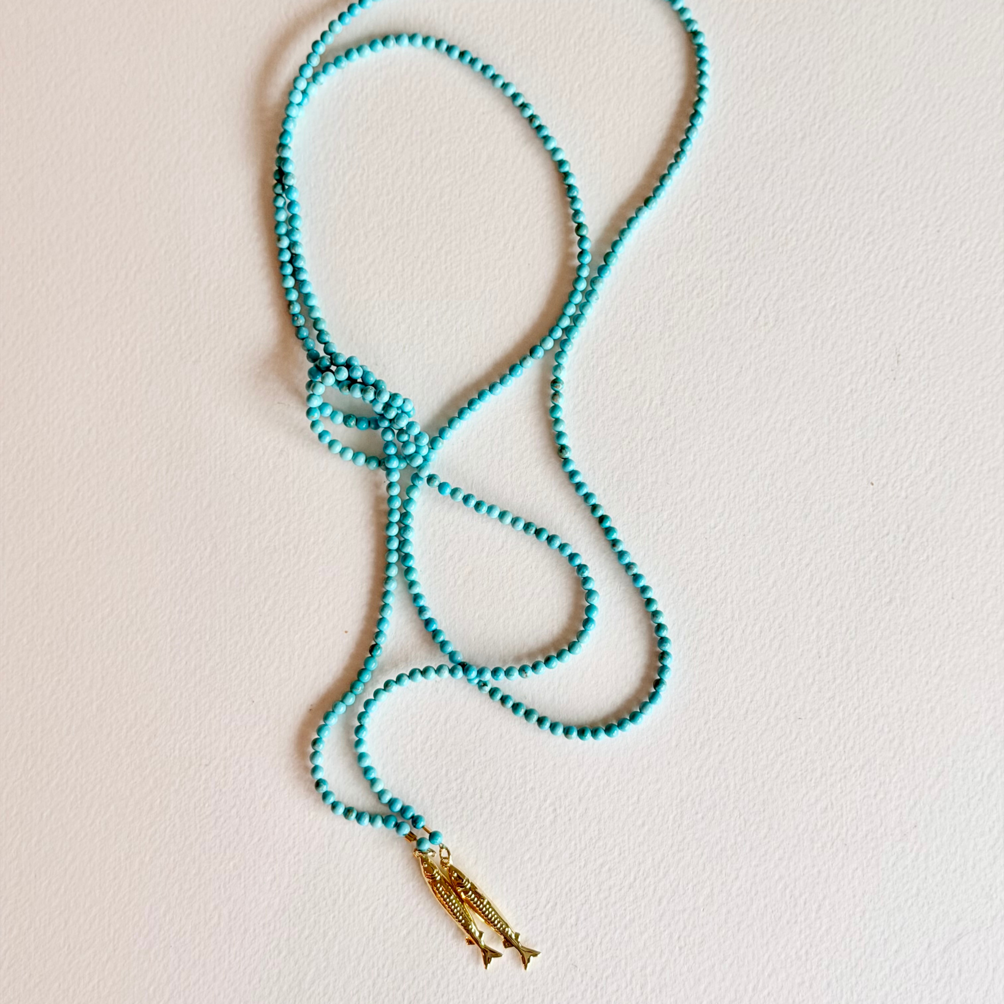 Turquoise beaded necklace with a gold pendant on a light beige background
