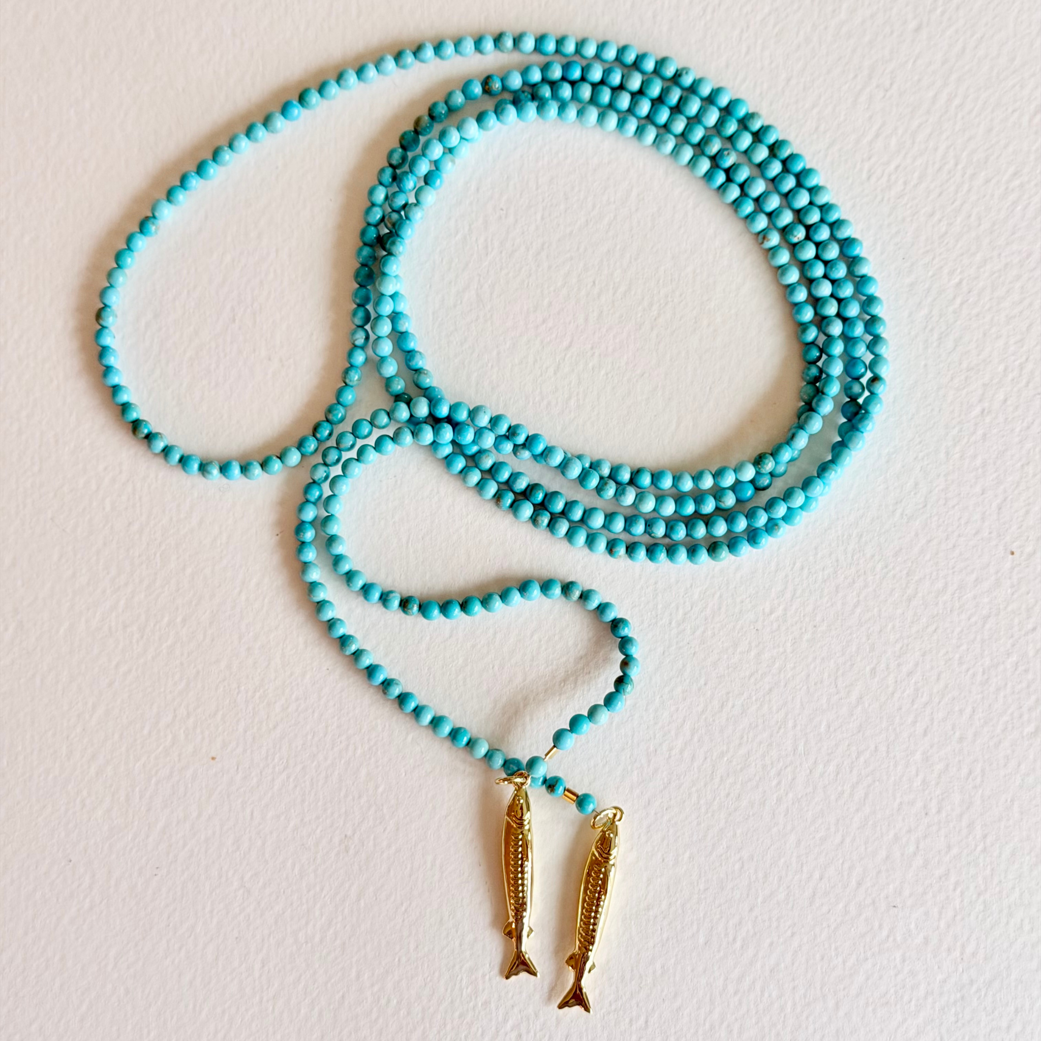 Turquoise beaded necklace with gold fish pendants on a light background