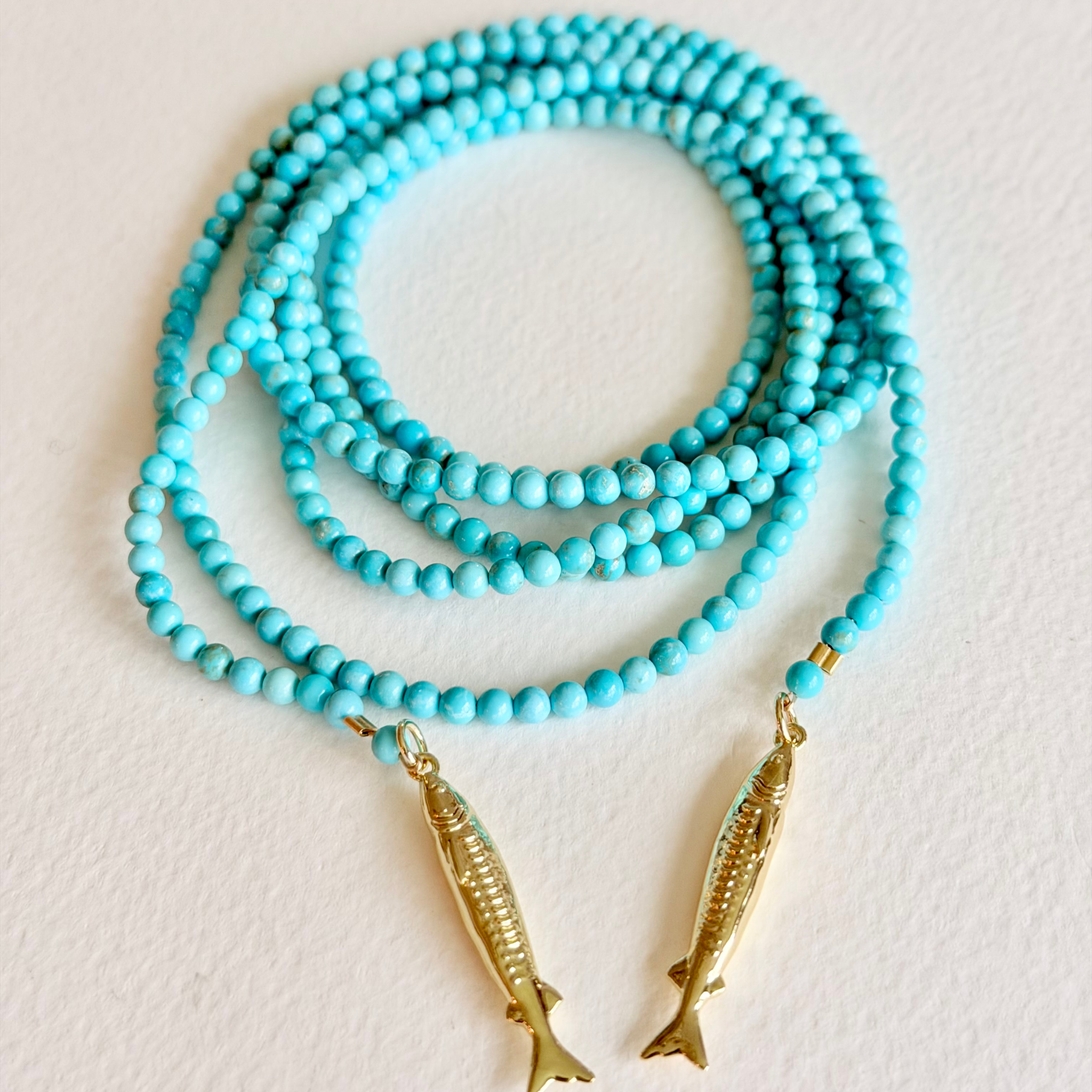 Turquoise beaded necklace with gold fish pendants on a light background
