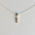A delicate silver chain necklace featuring a small fish charm wrapped in silver wire, accented by a tiny turquoise bead and a white pearl, displayed on a textured white background.