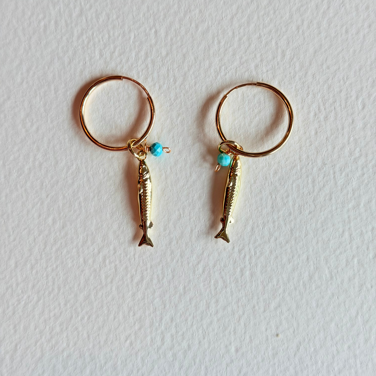 Gold fish-shaped earrings with turquoise beads on a white background