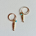 Gold hoop earrings with fish charms on a light gray background