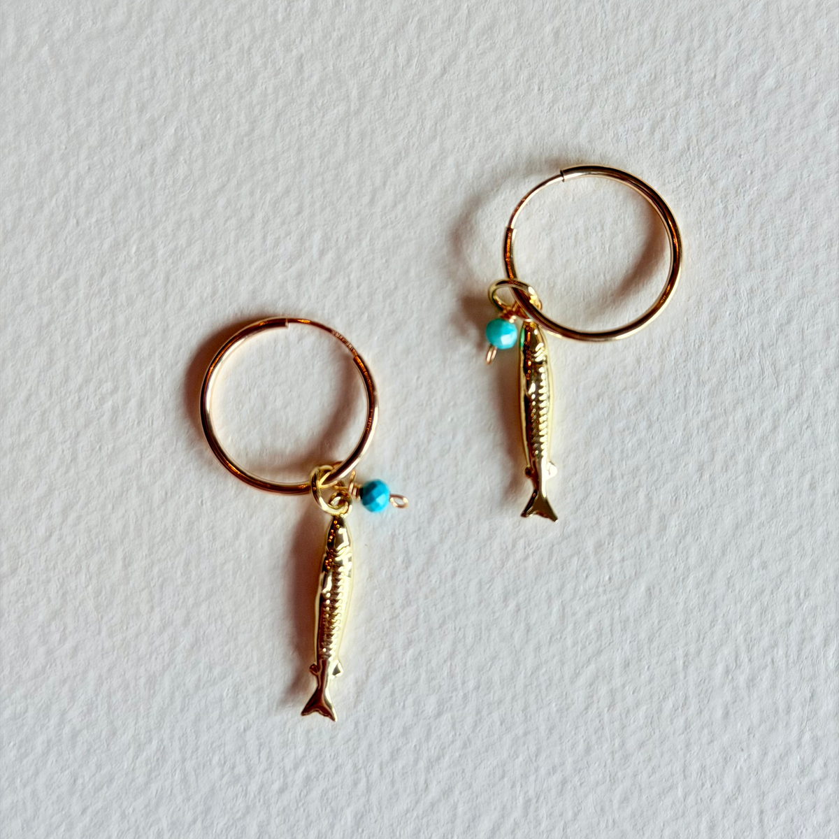 Gold hoop earrings with fish charms on a light gray background