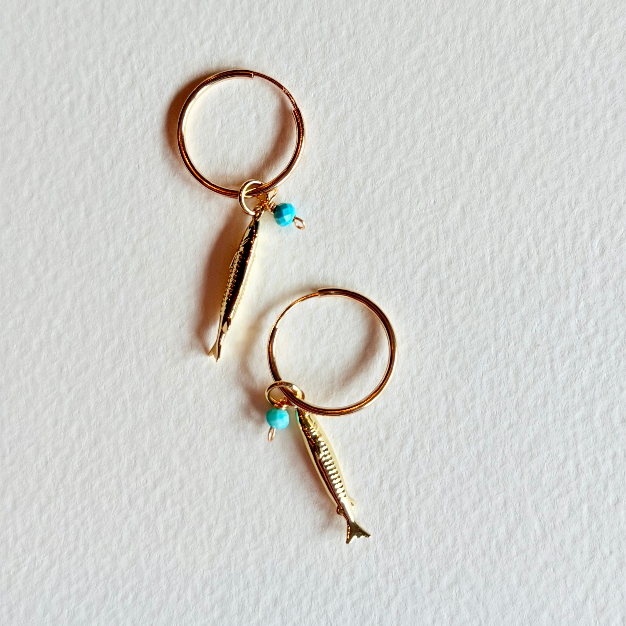 Gold hoop earrings with fish charms on a light gray background