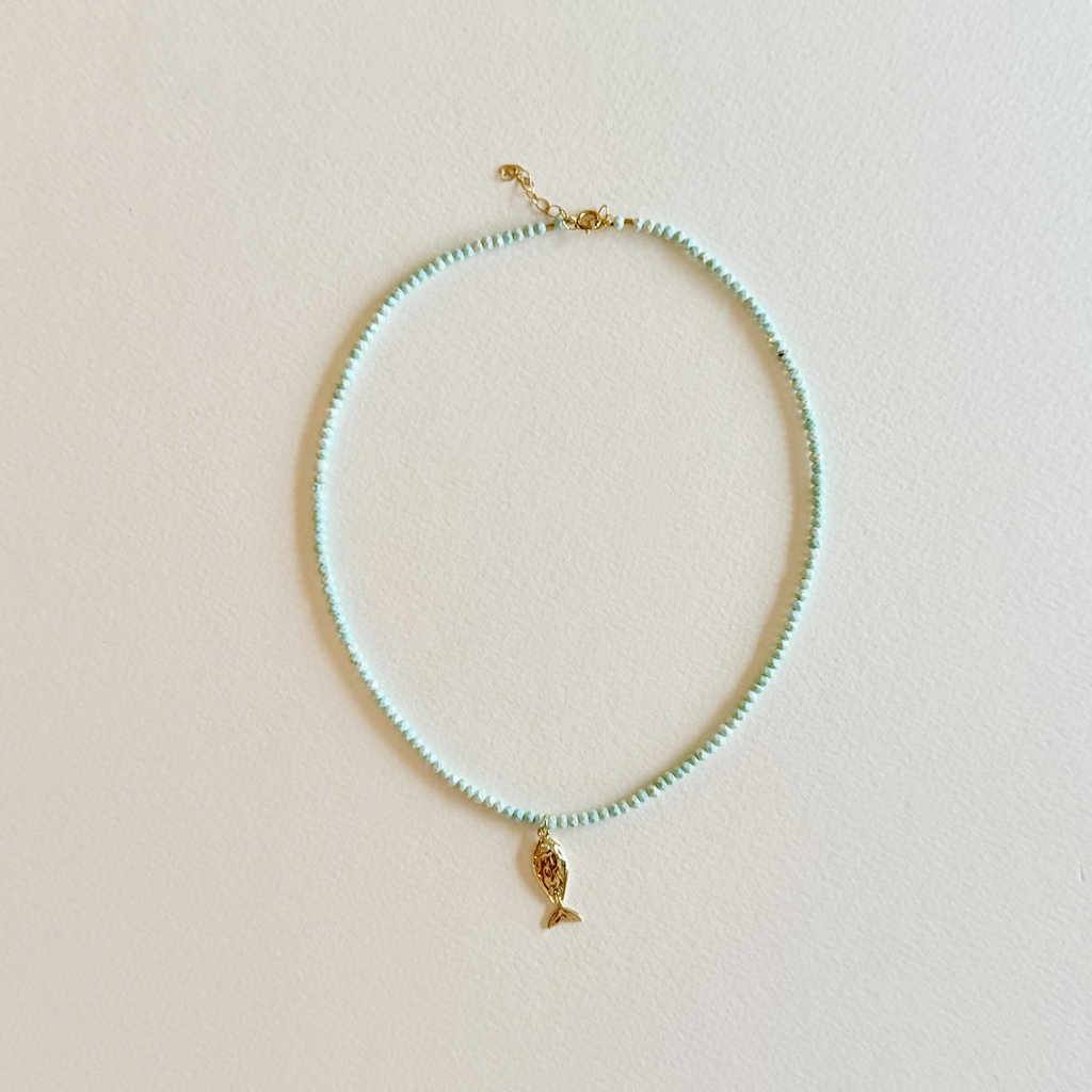 Handmade aqua turquoise beaded necklace with a signature gold fish charm and 14k gold-filled clasp, measuring 16 inches with a 2-inch extender. Inspired by the colors of the sea and handcrafted by Marie & Oakley.