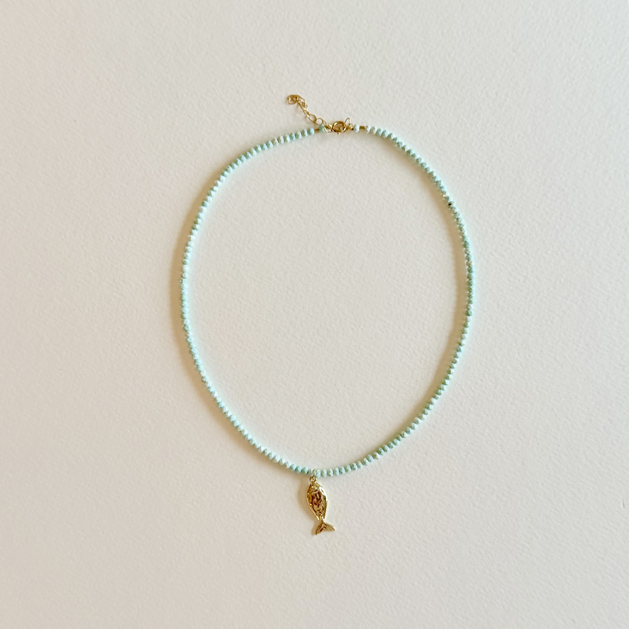 Handmade aqua turquoise beaded necklace with a signature gold fish charm and 14k gold-filled clasp, measuring 16 inches with a 2-inch extender. Inspired by the colors of the sea and handcrafted by Marie & Oakley.
