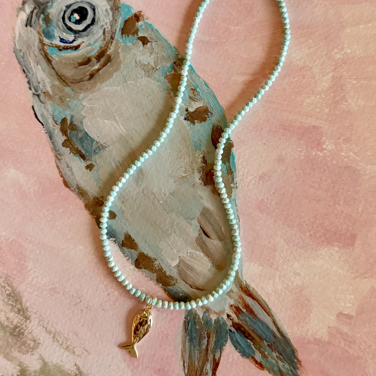 Handmade aqua turquoise beaded necklace with a signature gold fish charm and 14k gold-filled clasp, measuring 16 inches with a 2-inch extender. Inspired by the colors of the sea and handcrafted by Marie & Oakley.