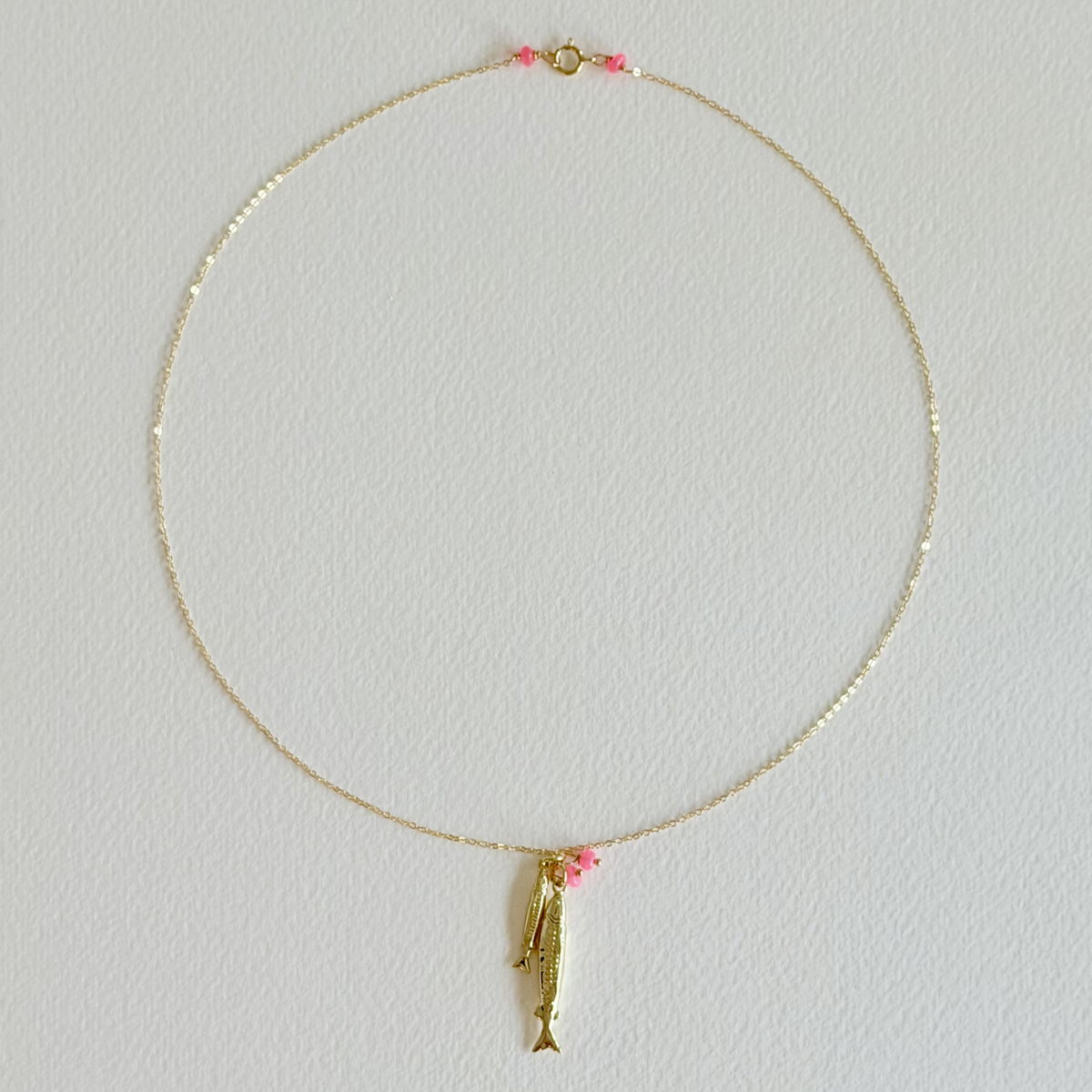 Gold necklace with a fish pendant on a light gray background