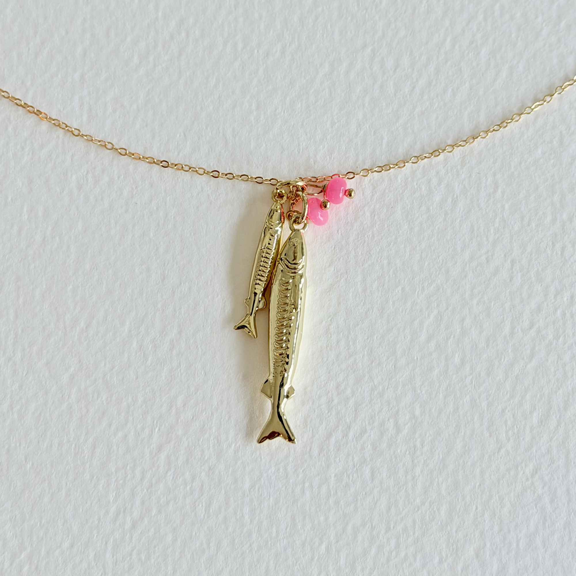 Gold fish-shaped pendant necklace with pink beads on a light gray background