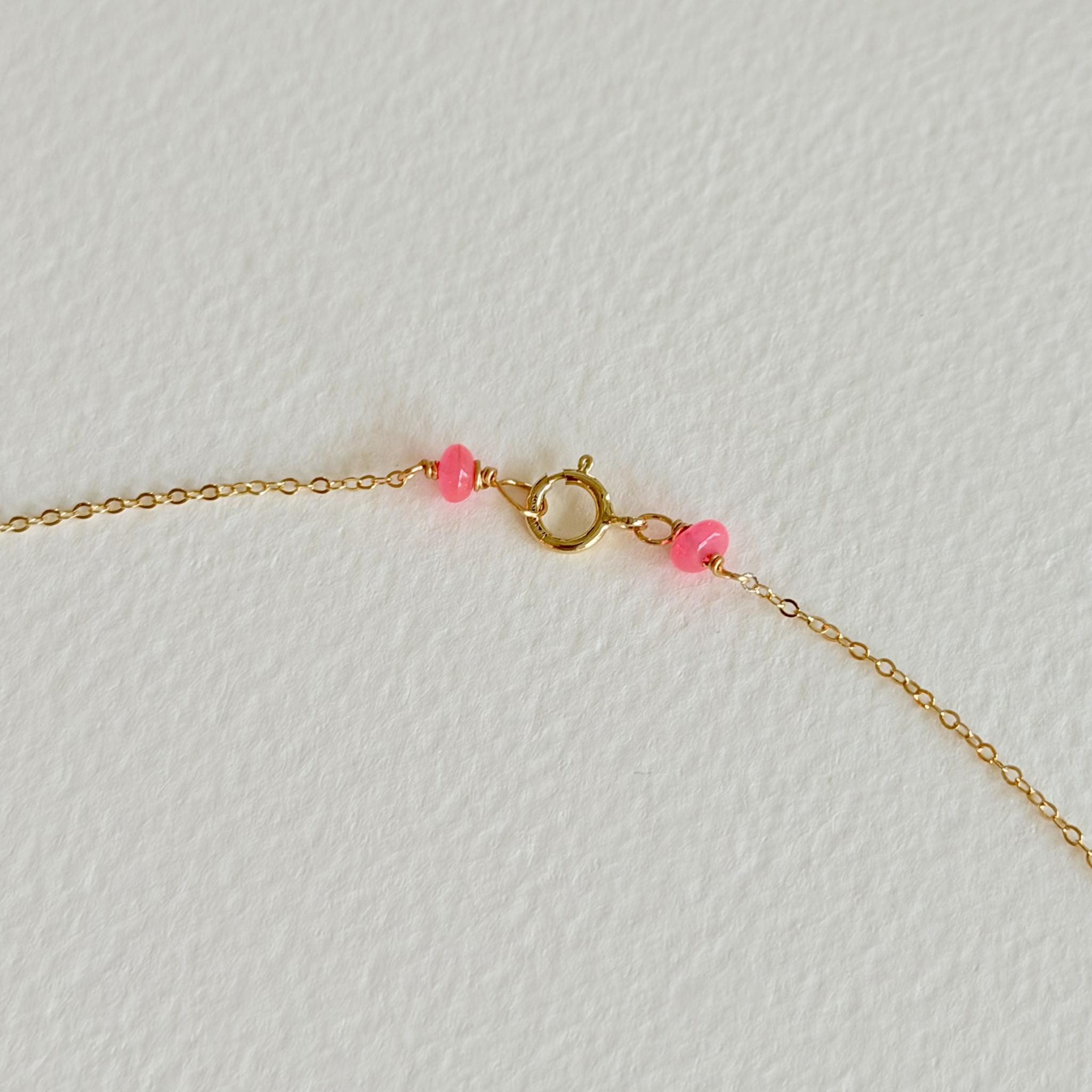 Gold bracelet with pink beads on a light gray background