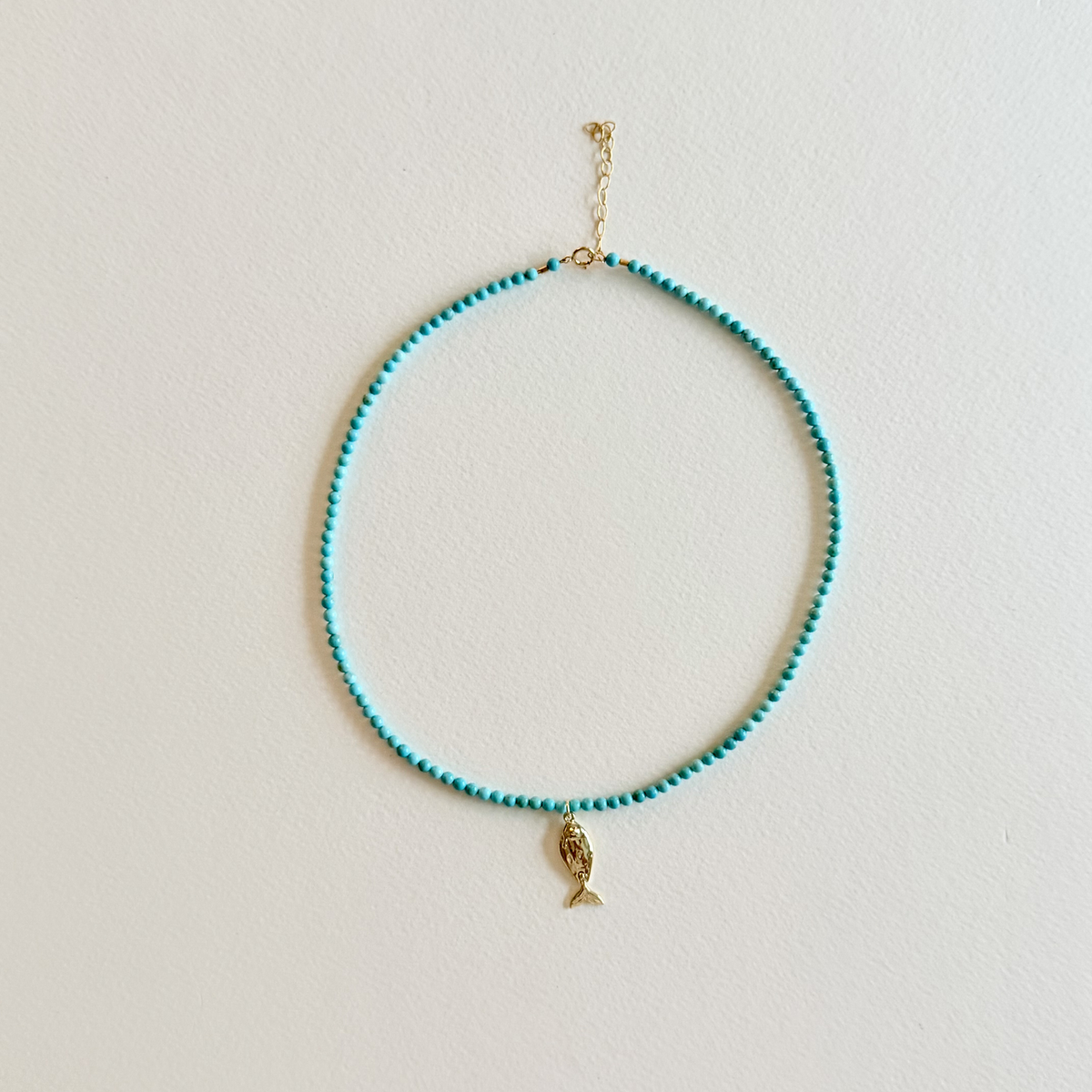 Little Catch Smooth Turquoise Necklace on light textured paper.