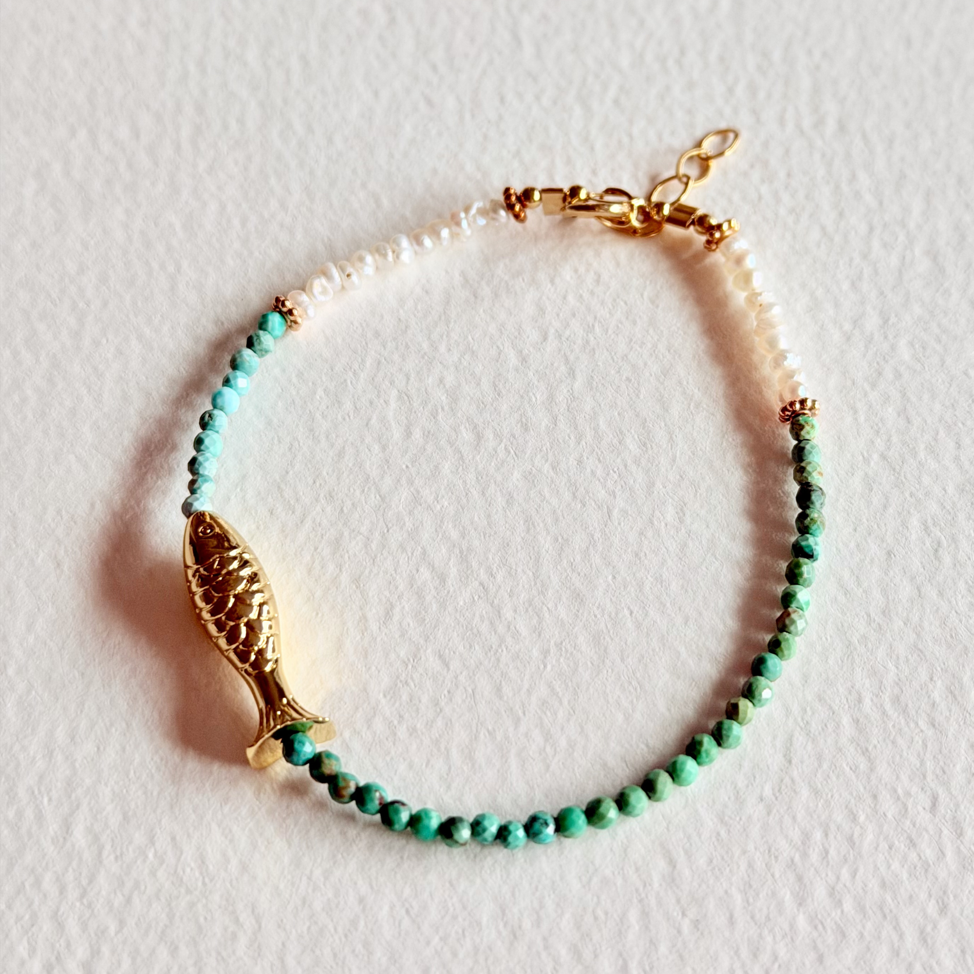 Bracelet with turquoise beads and gold fish charm on a light background