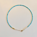 Turquoise beaded necklace with a gold clasp on a beige background