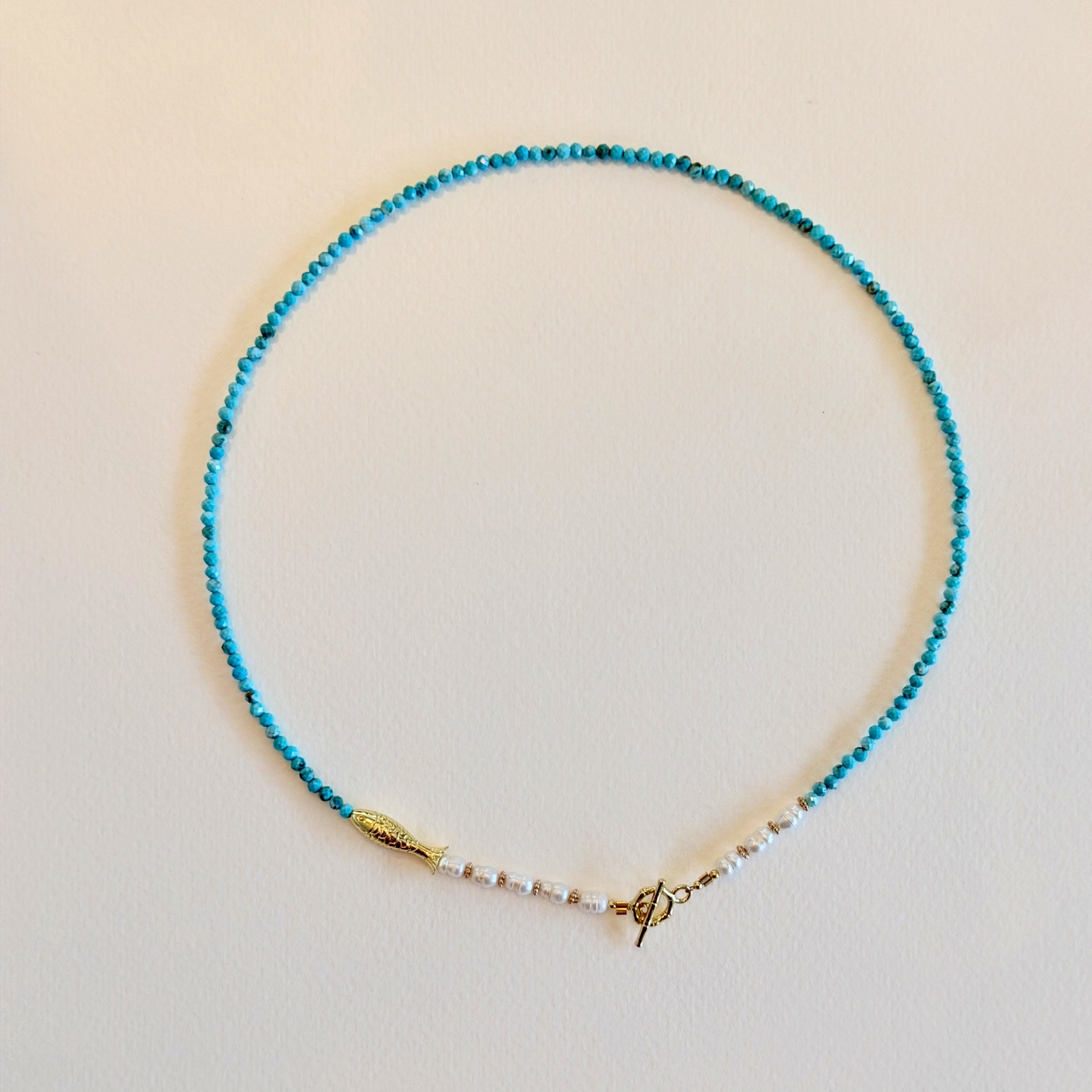 Turquoise beaded necklace with a gold clasp on a beige background