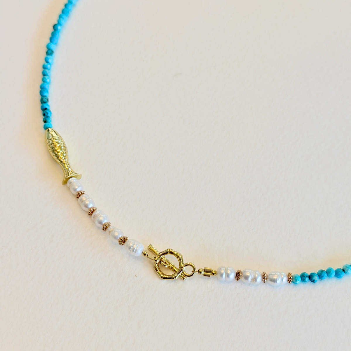 Necklace with turquoise beads and gold clasp on a beige background