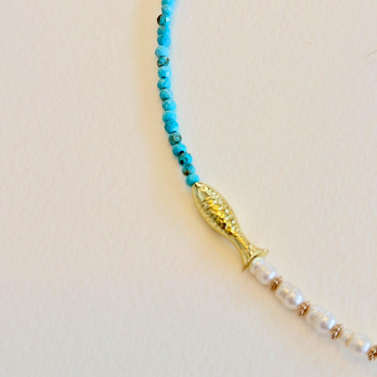 Necklace with blue beads, gold fish bead, and white pearls on a beige background