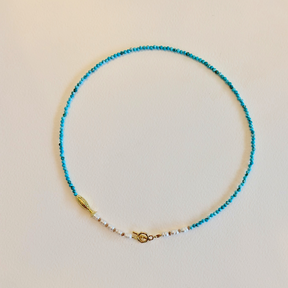 Turquoise beaded necklace with a gold clasp on a beige background