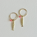 Gold hoop earrings with fish charms on a light gray background