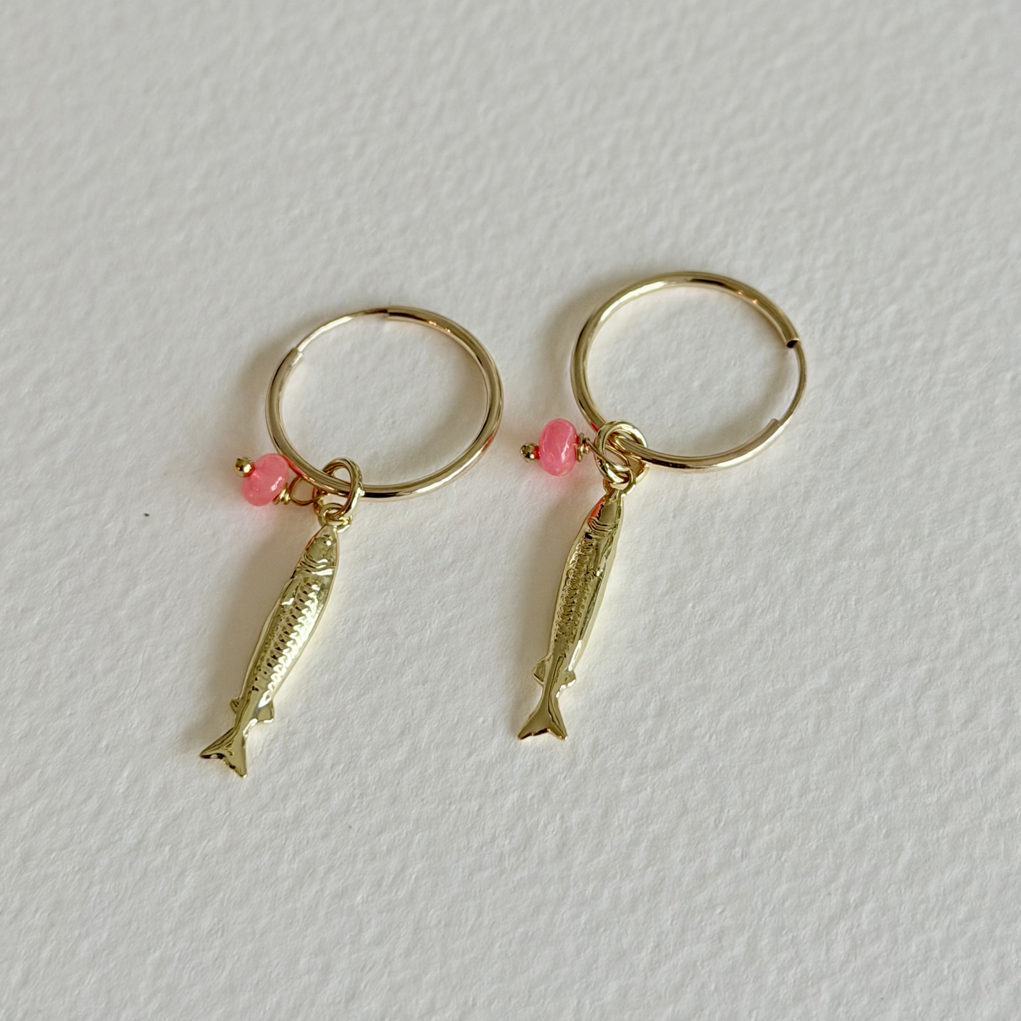 Gold fish-shaped earrings with pink beads on a white background