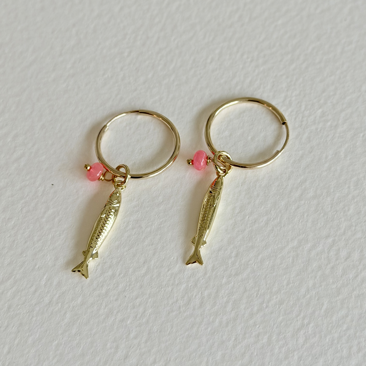 Gold fish-shaped earrings with pink beads on a white background