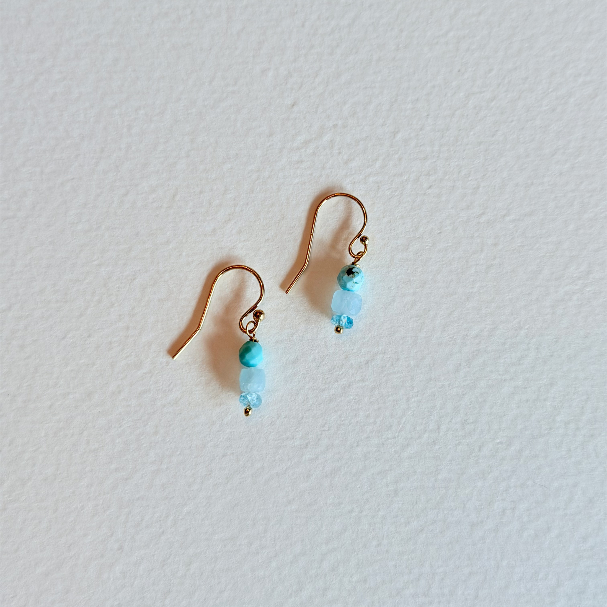 Pair of gold earrings with turquoise beads on a light gray background