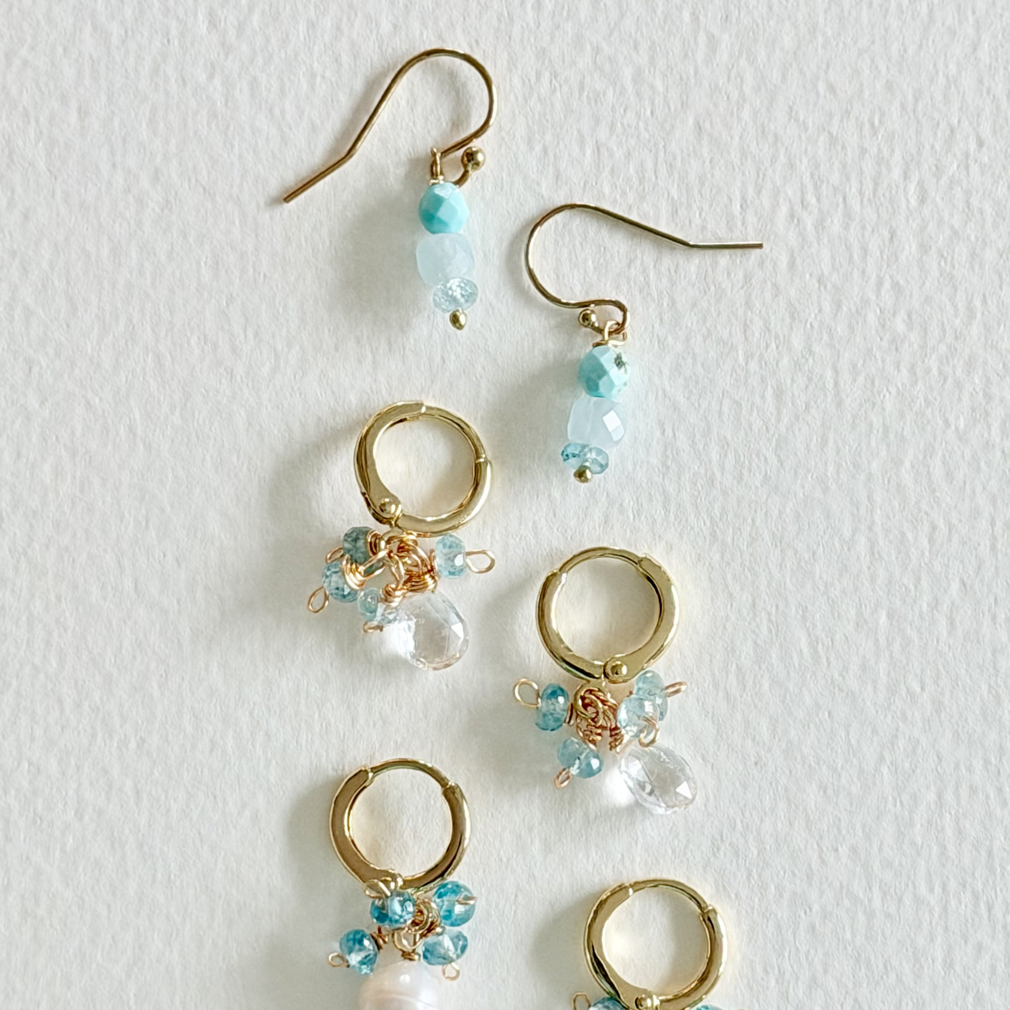 Gold hoop earrings with blue and clear beads on a light gray background